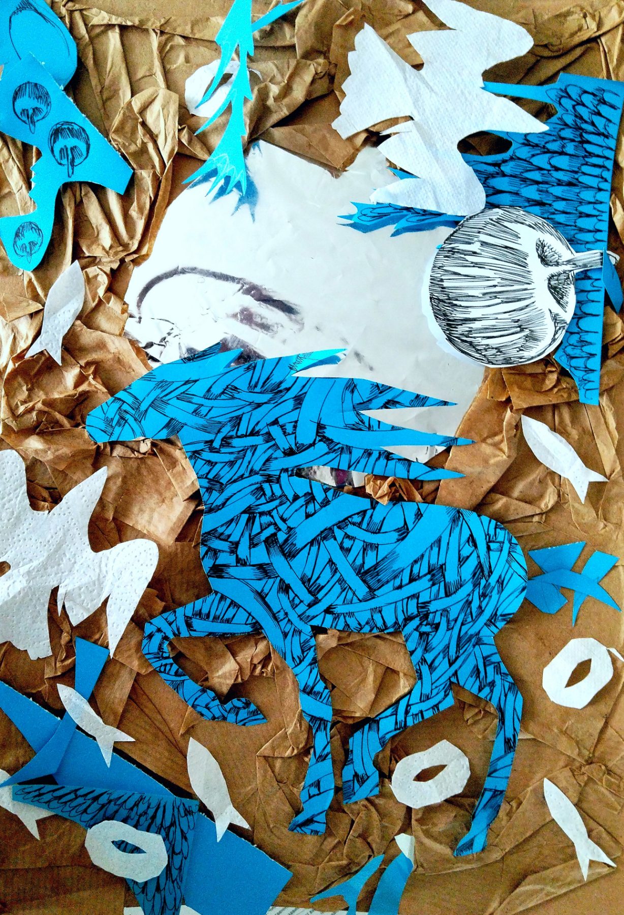 A ground of crumpled brown kraft paper. A large horse or deer, cut from blue paper printed with dense black hatching, stands in the centre; a round hatched head floats at its shoulder against a blue panel of drawn feathers. White napkin birds and small white fish drift across the brown, and a photographed face lies half-buried at the upper left, its mouth just visible.